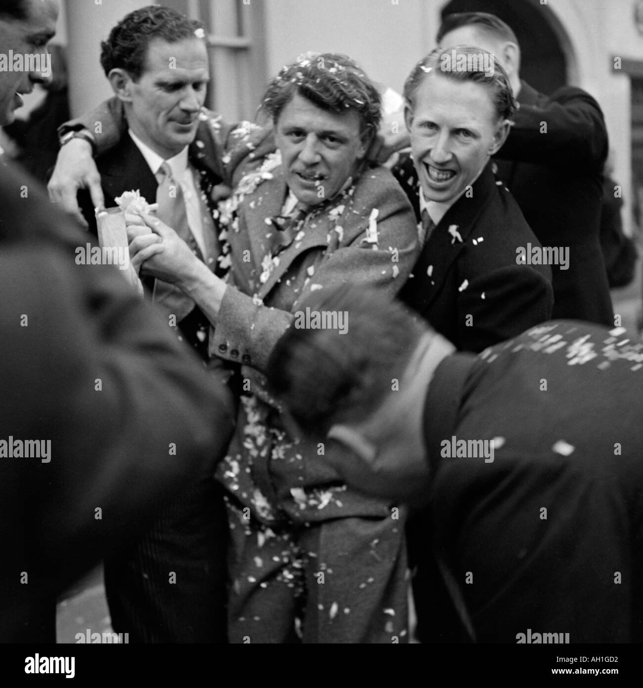 OLD VINTAGE FAMILY PHOTOGRAPH SNAP SHOT OF GUESTS THROWING CONFETTI AT BRIDEGROOM AFTER WEDDING CEREMONY CIRCA 1950 Stock Photo