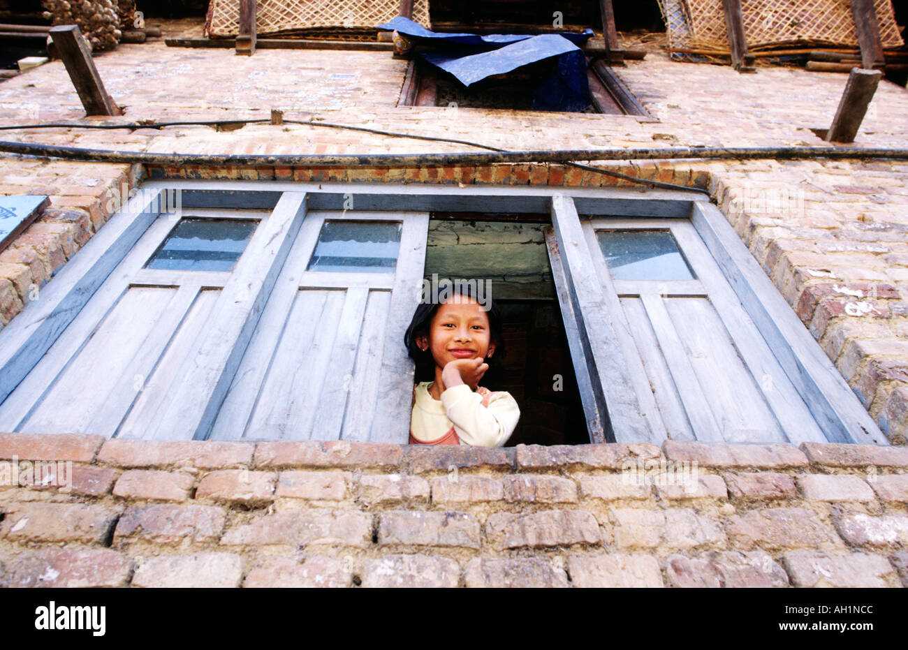 One young Nepalese girl looking down from blue painted window from the 2nd level of her home Kathmandu Valley Stock Photo