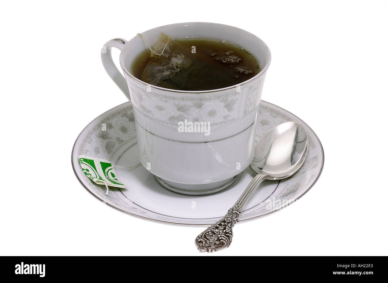 black tea with tea bag in white tea cup saucer teaspoon silhouetted on