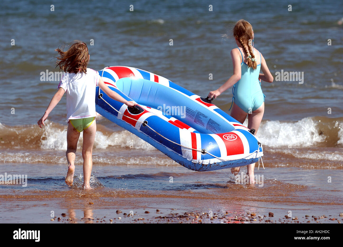 Two young girls carry an inflatable dinghy into the sea Stock Photo Alamy