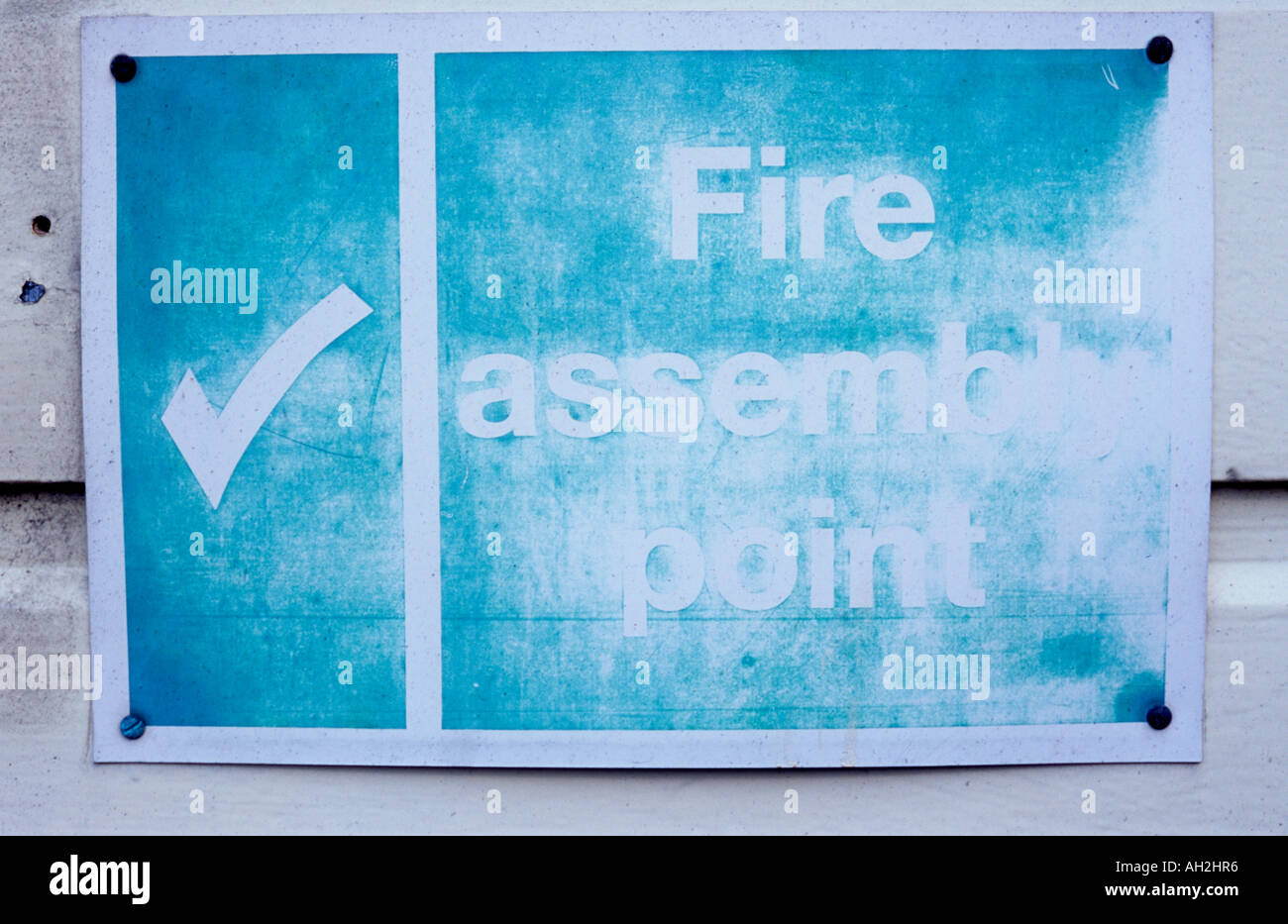 Close up of a very faded and weathered plastic white and green sign on white weatherboarding stating Fire assembly point Stock Photo