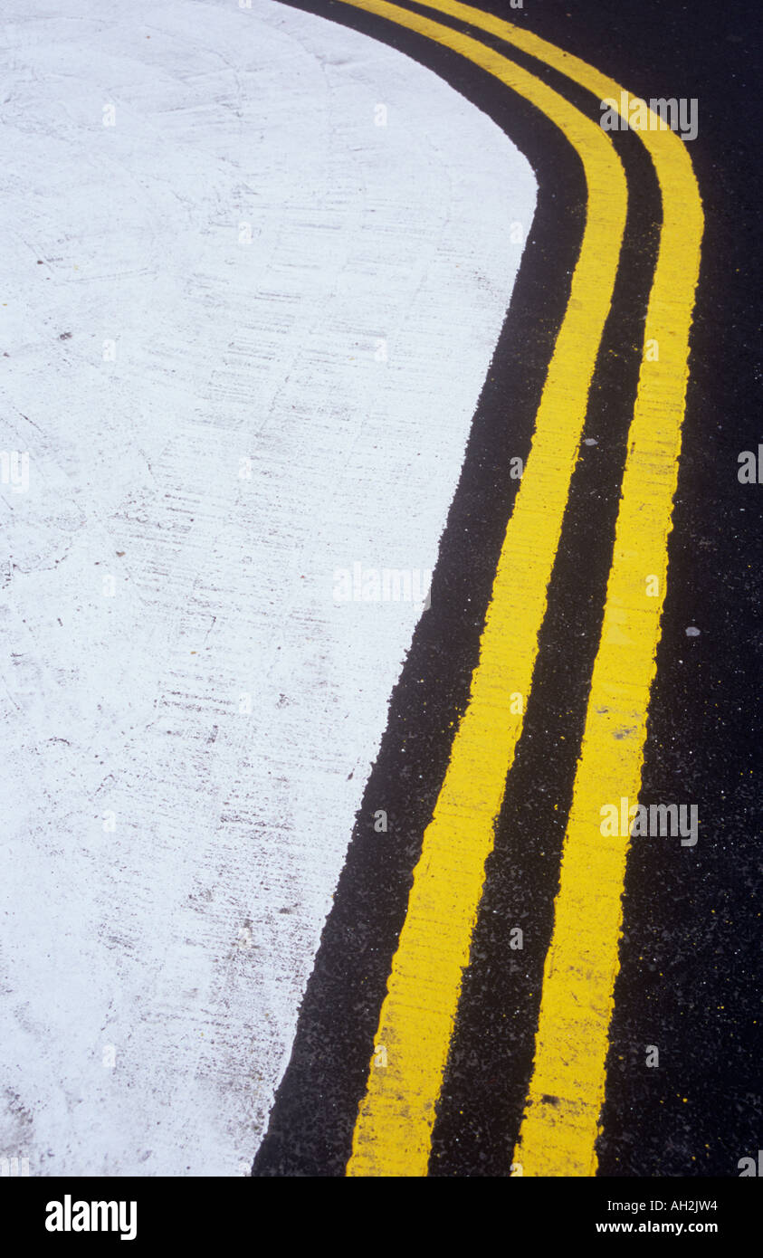 Detail of freshly painted double yellow lines curving around a white painted no access area on new tarmac Stock Photo