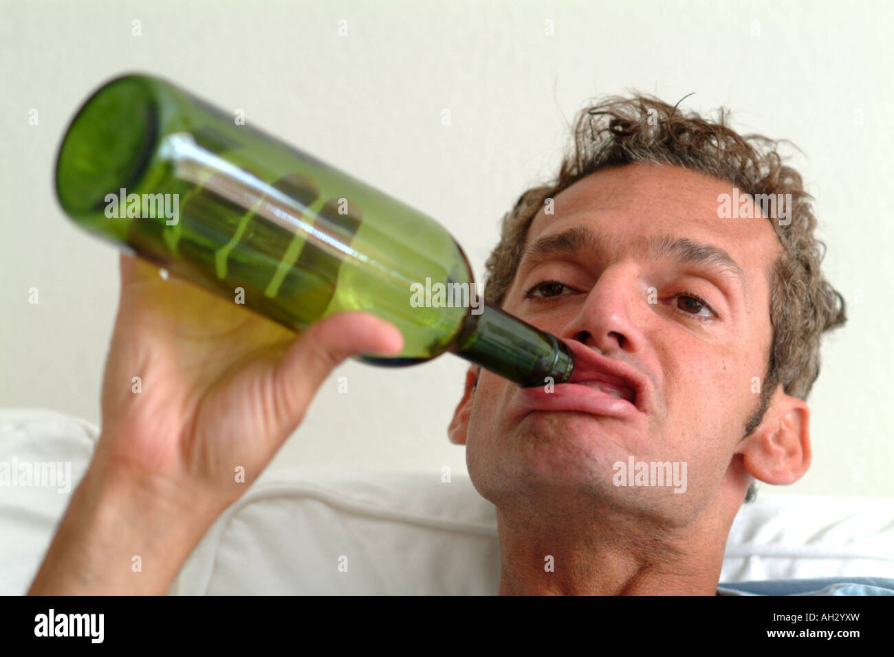 A man holding an empty bottle of wine to his mouth with a silly expression on his face Stock