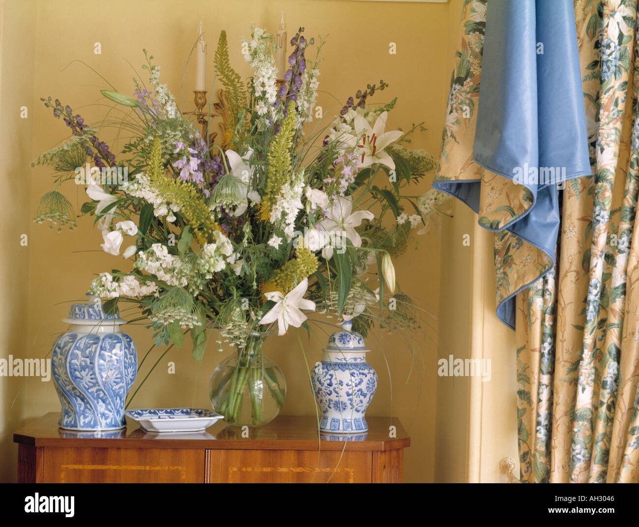 Close-up of white lilies and blue delphiniums in vase on chest with ...