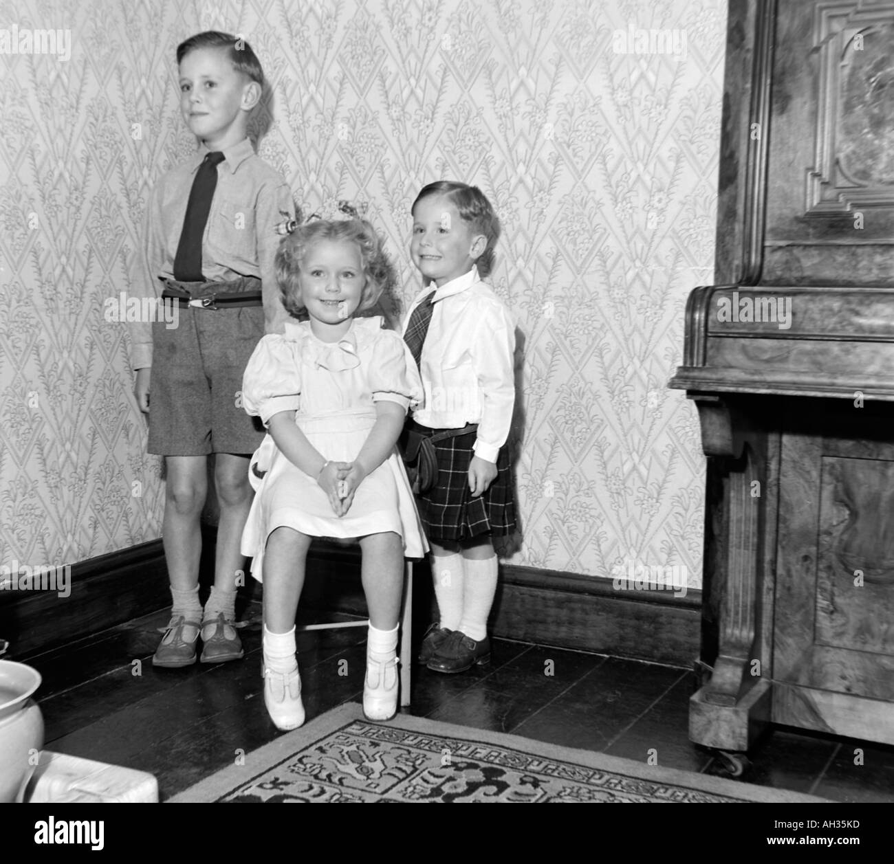 OLD VINTAGE FAMILY SNAPSHOT PHOTOGRAPH OF TWO YOUNG BOYS AND YOUNG GIRL SITING ON SOFA Stock Photo