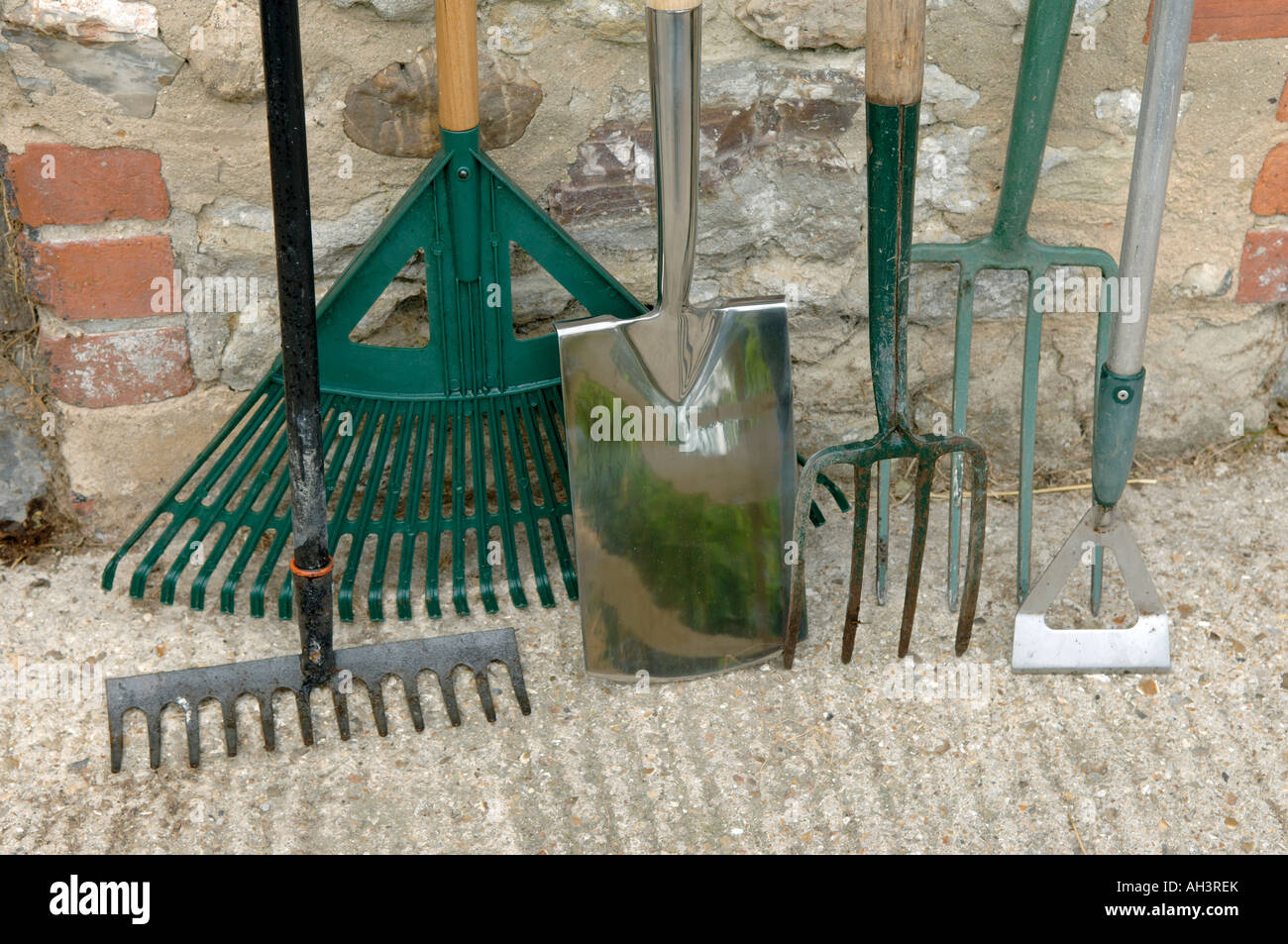 Garden tools spade hoe forks and rakes leaning against an outhouse wall