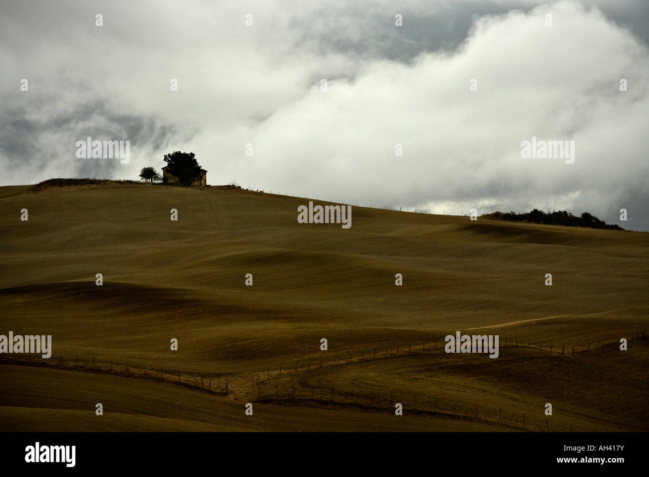 Farmhouse atop undulating fields, with stormy sky, Val d'Orcia, Tuscany, Italy Stock Photo