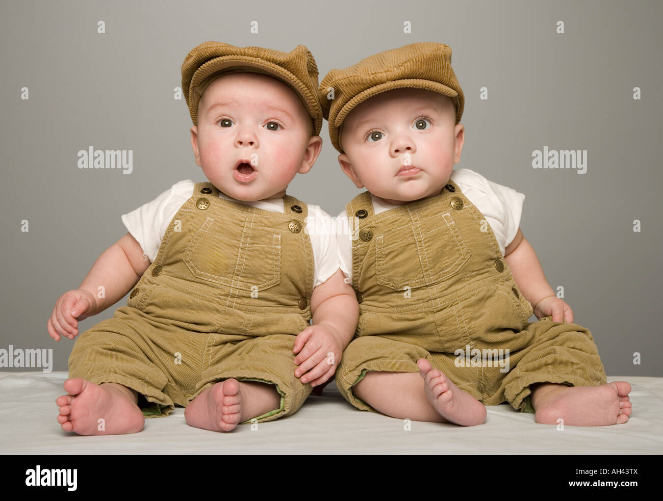 Two babies in matching hat and overalls Stock Photo Alamy