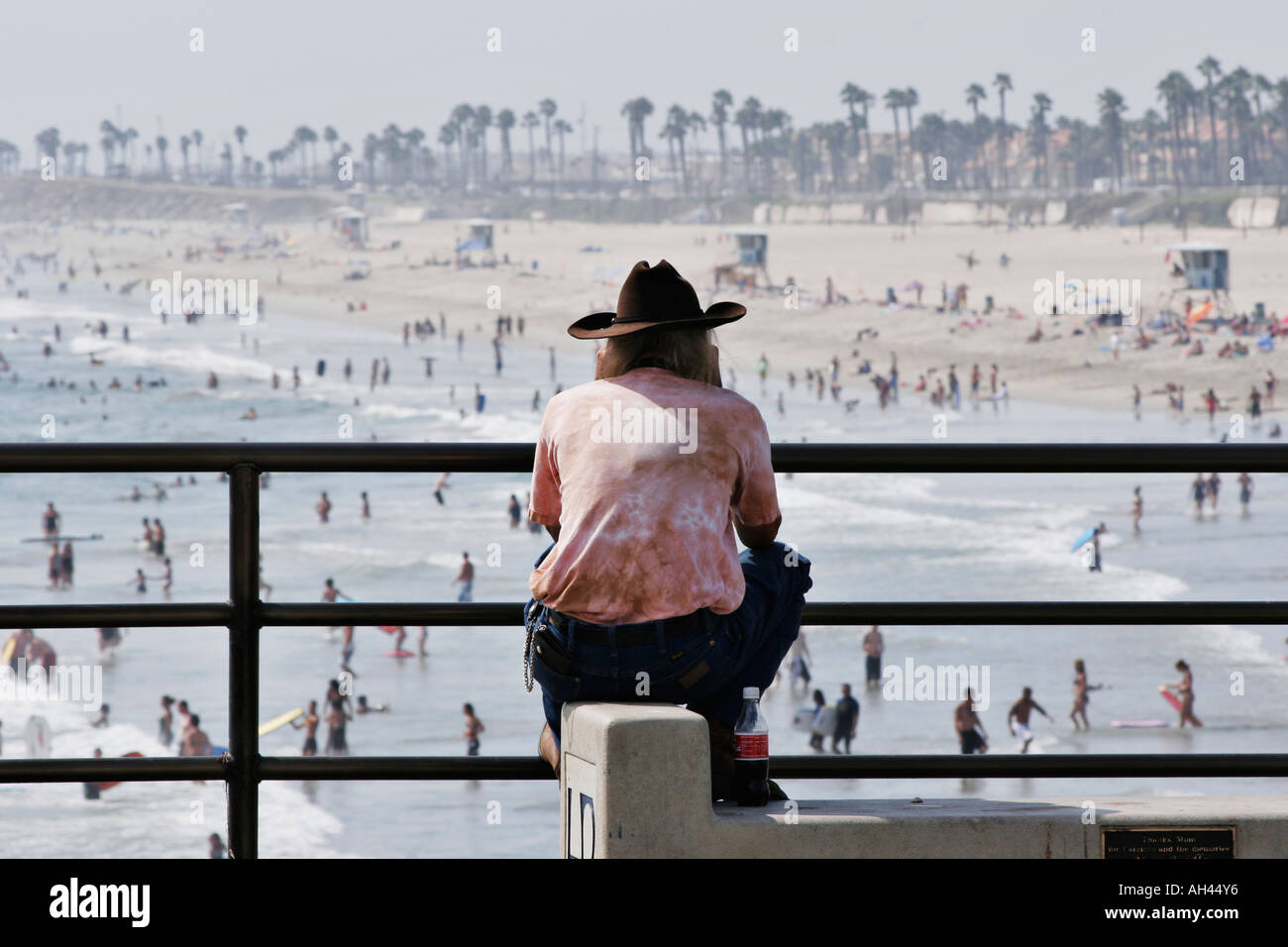 A man sitting on the pier in Huntington Beach California, watching the beach goers Stock Photo picture