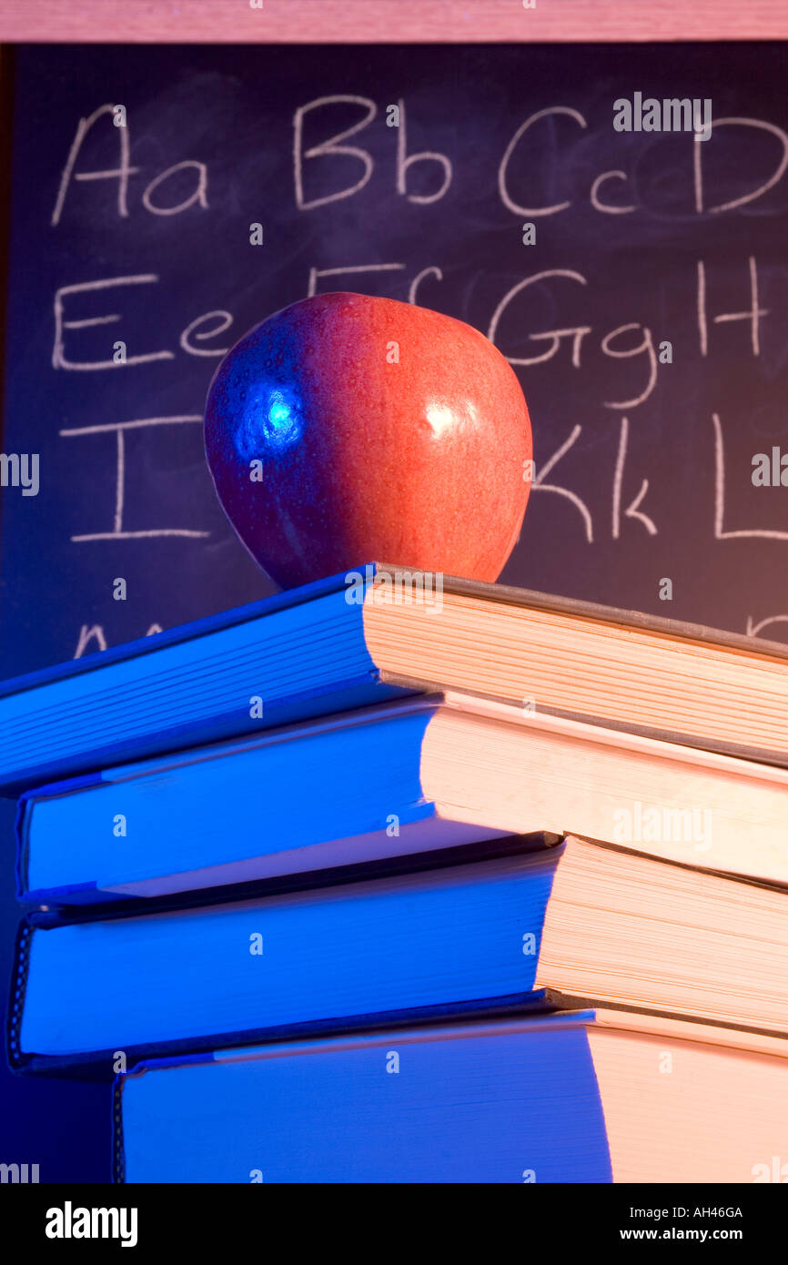 Apple on books in front of a chalkboard with the alphabet written on it. Stock Photo