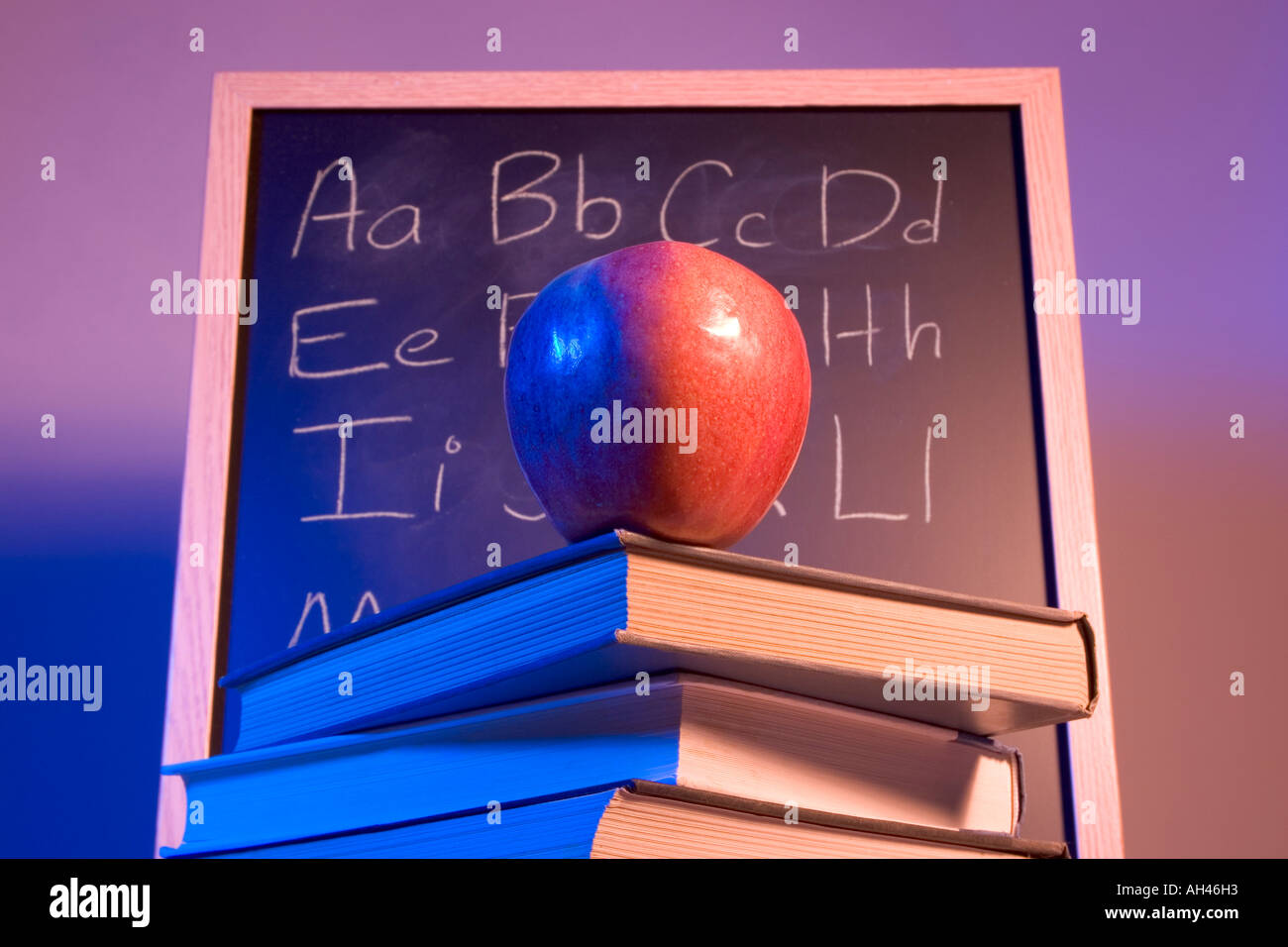 Apple on books in front of a chalkboard with the alphabet written on it. Stock Photo