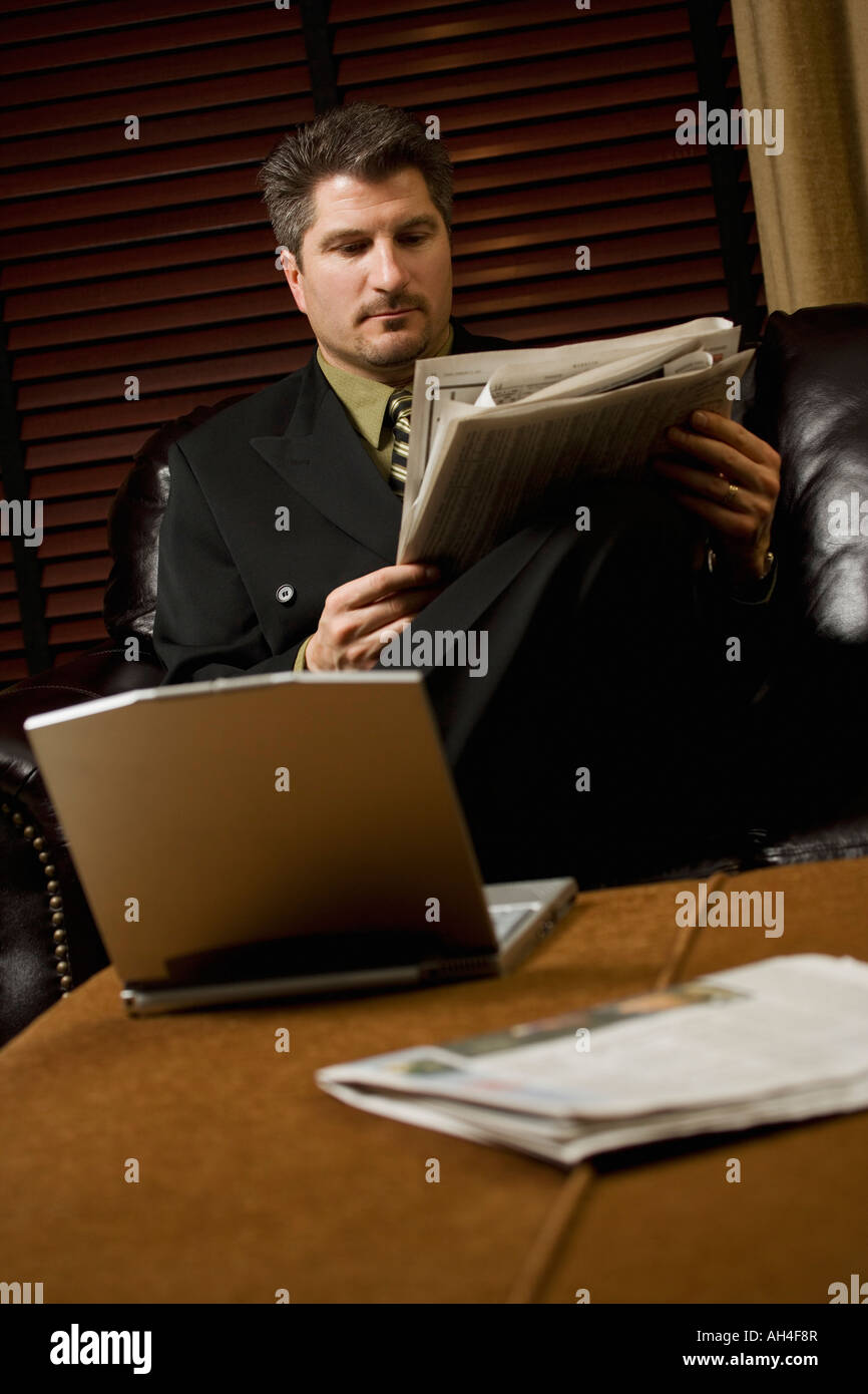 Businessman reading the newspaper with his laptop Stock Photo