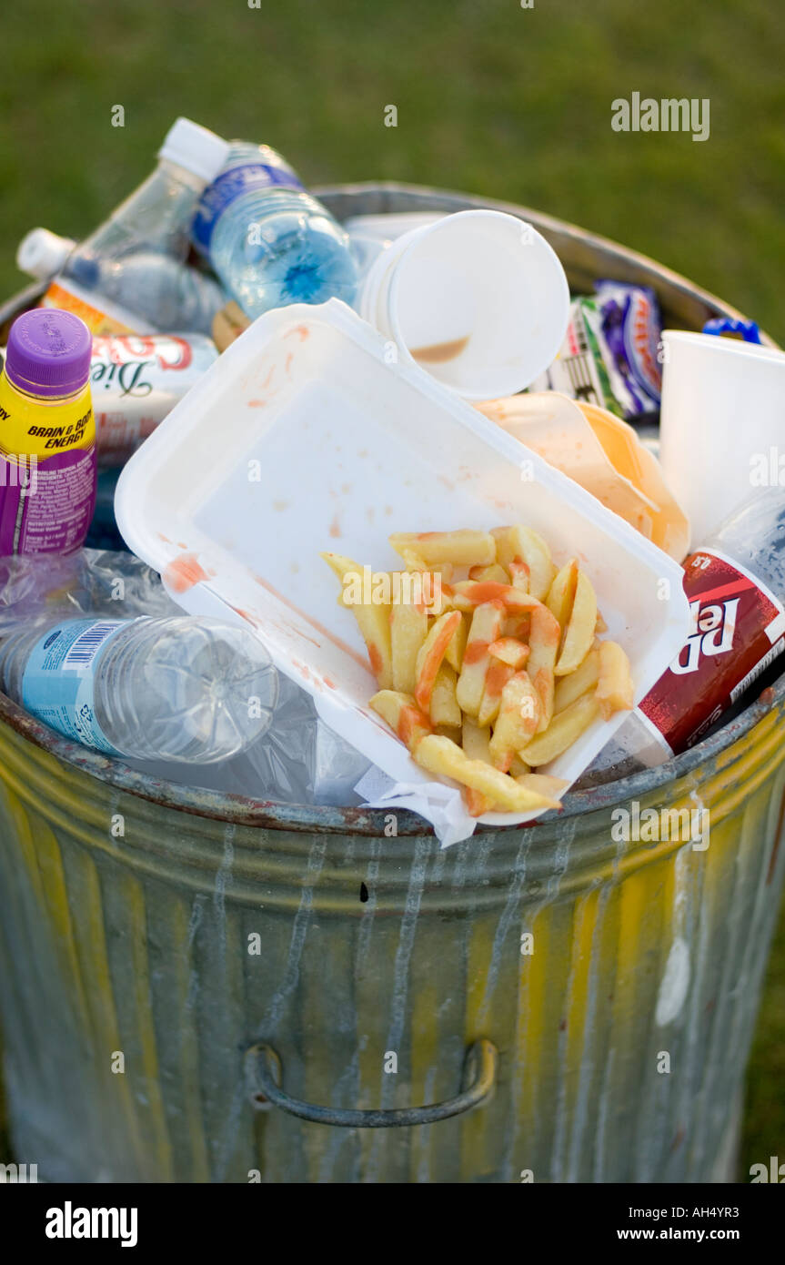 A metal Rubbish trash can overflowing with waste chips food plastic