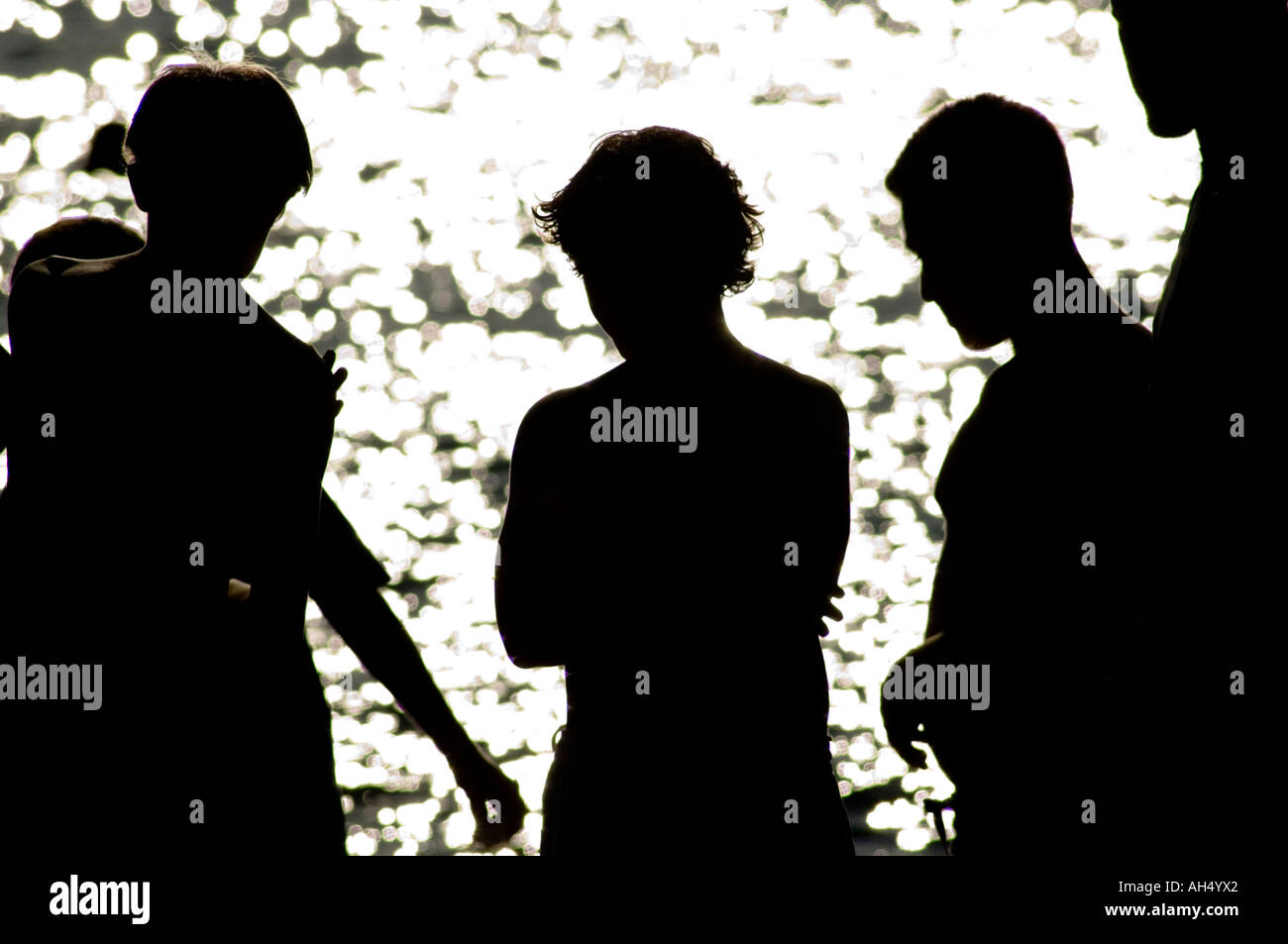 silhouettes of 4 5 young teenage boys against a dazzling sea Stock Photo