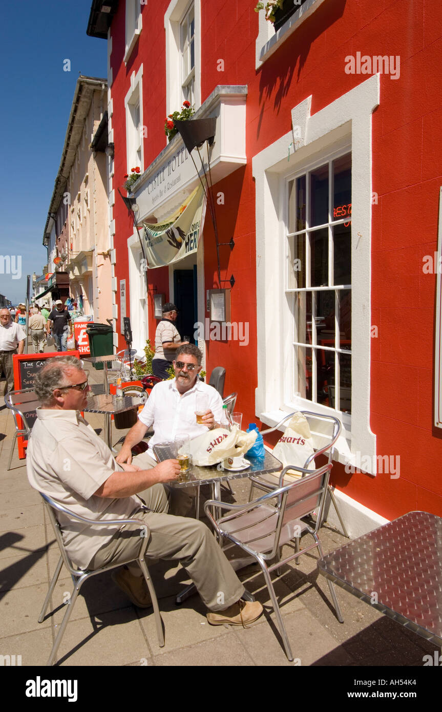 two men sitting and drinking beer outside the red painted Castle Hotel,  Aberaeron Ceredigion Cymru Wales summer afternoon Stock Photo