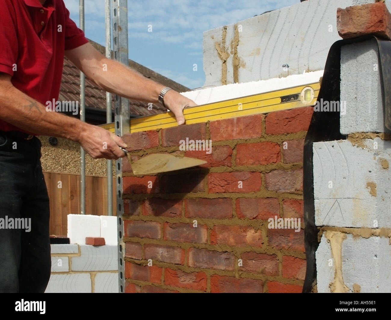 Building construction work in progress close up bricklayer using trowel & spirit level working on facing brick skin of cavity wall house building UK Stock Photo