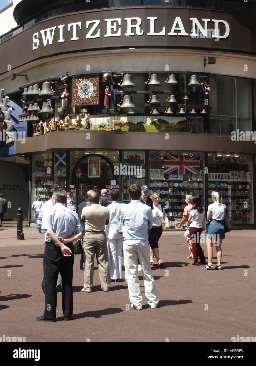 Street scene Swiss tourist information office shop & people watch revolving clock display of cows milkmaids & chiming bells Leicester Square London UK Stock Photo