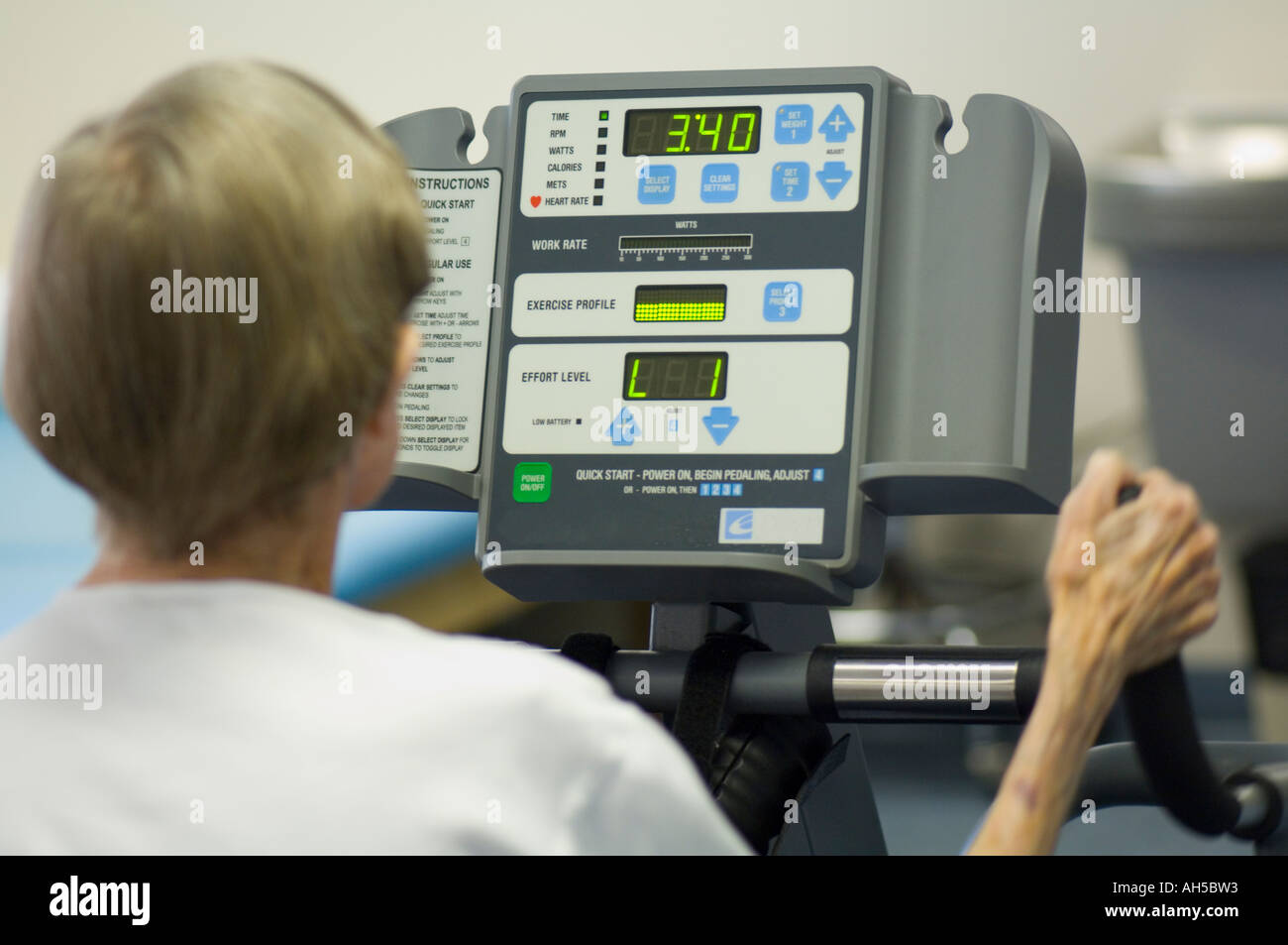 80 year old woman working out in gym on a digital exercise machine using oxygen Stock Photo