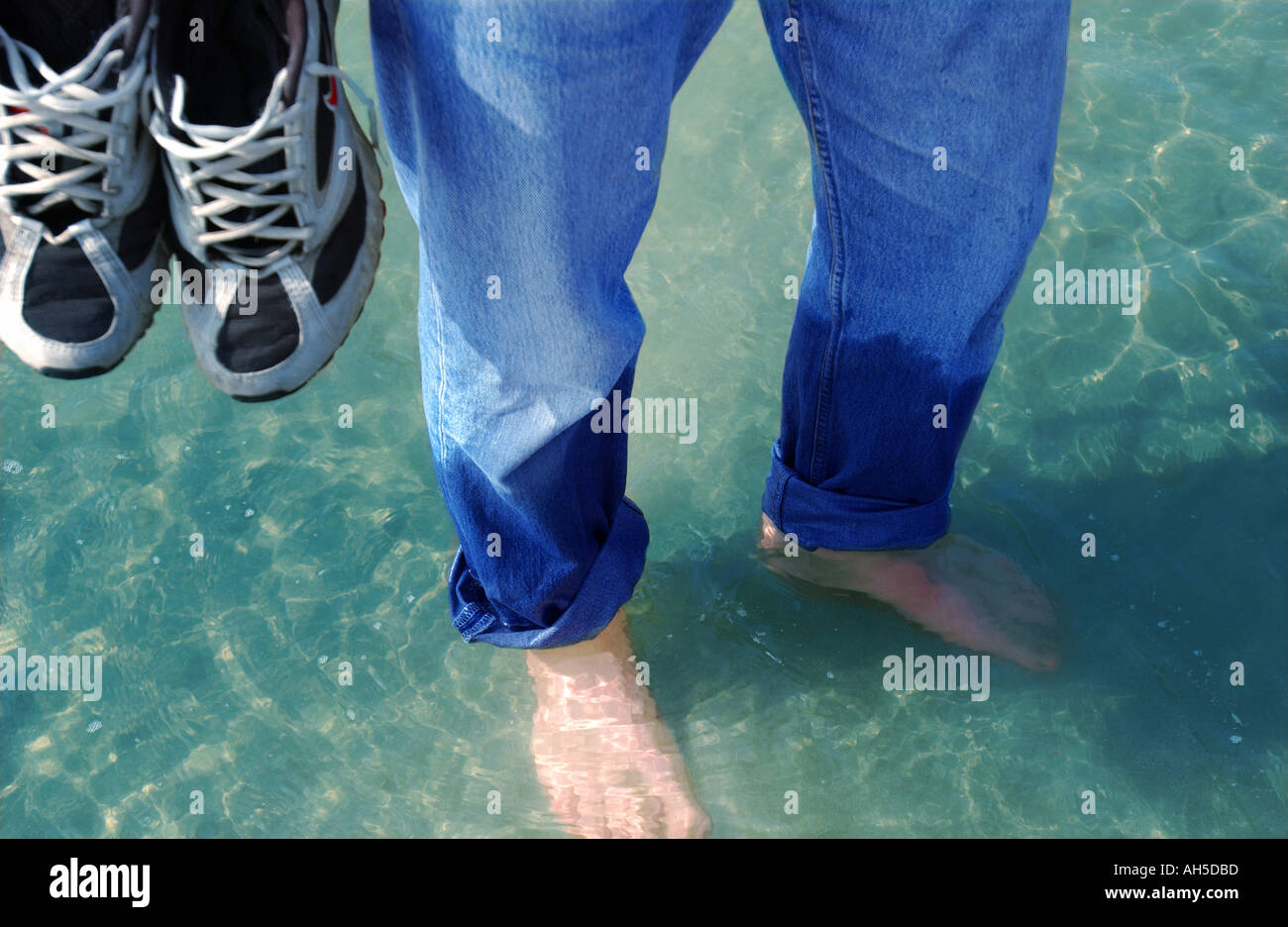 Male paddling in wet jeans in sea holding trousers Stock Photo