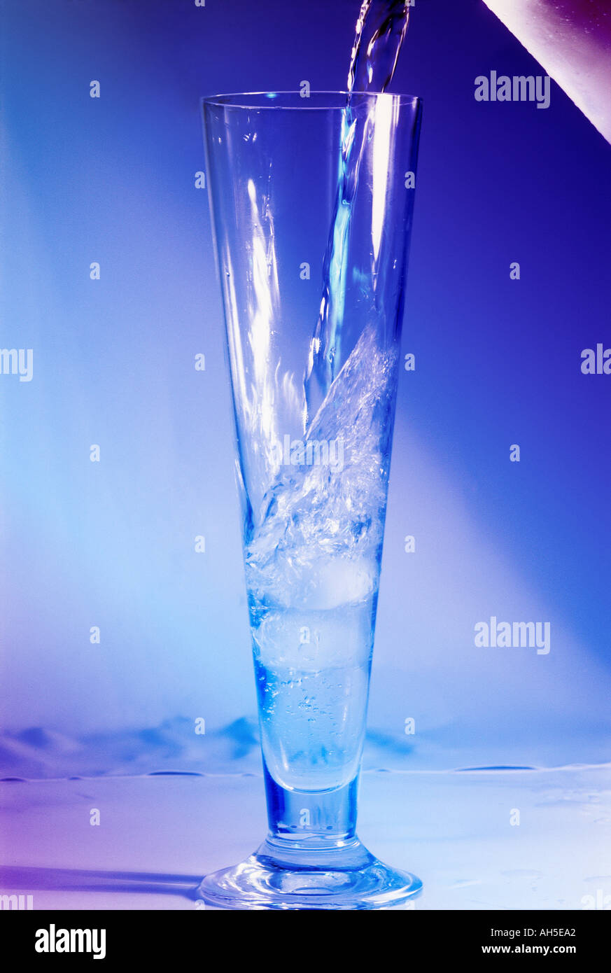 Water pouring into a tall glass with a blue and pink light Stock Photo