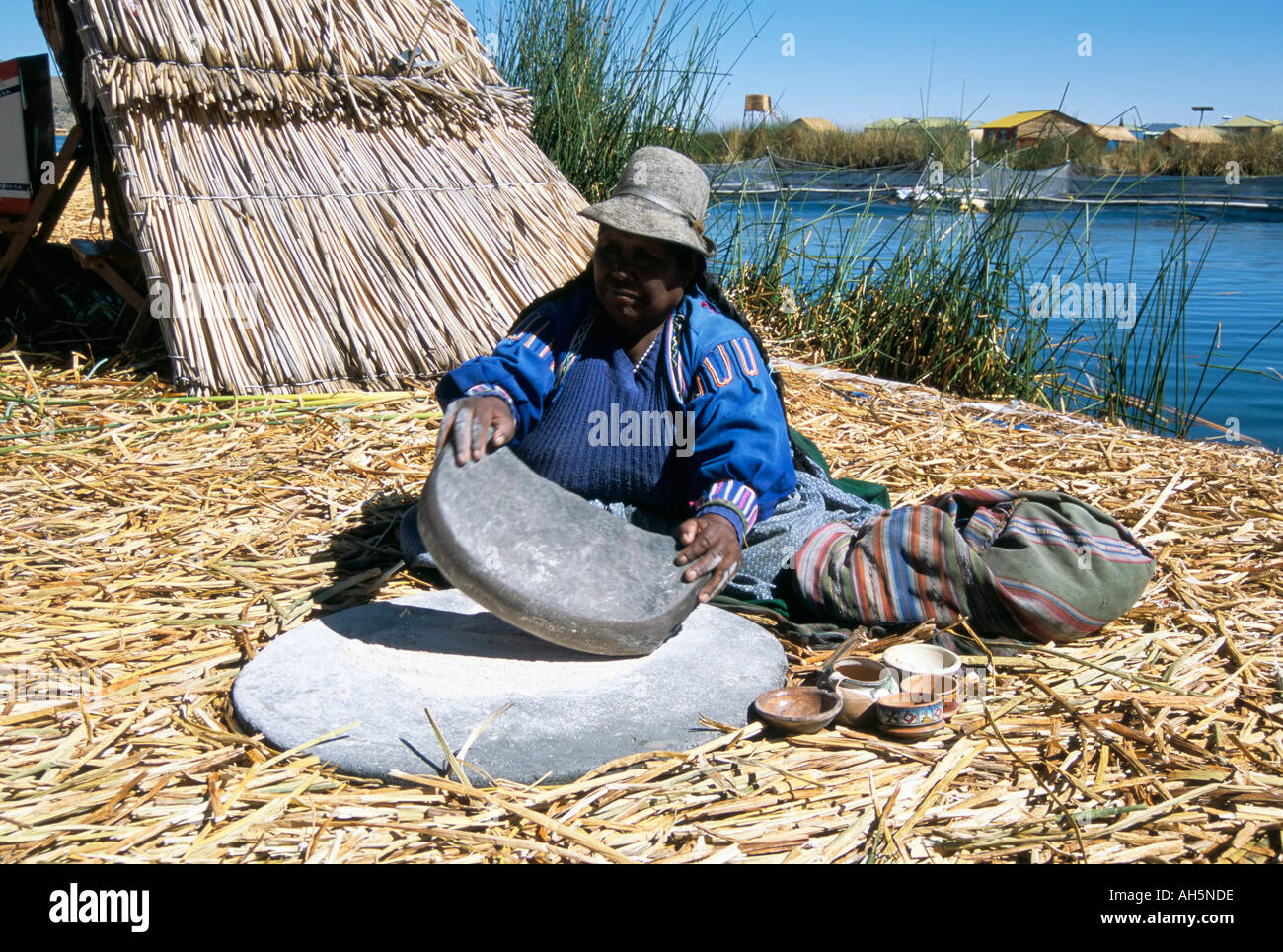 Uros Urus woman grinding corn Islas Flotantas reed islands Lake Titicaca Peru South America Stock Photo