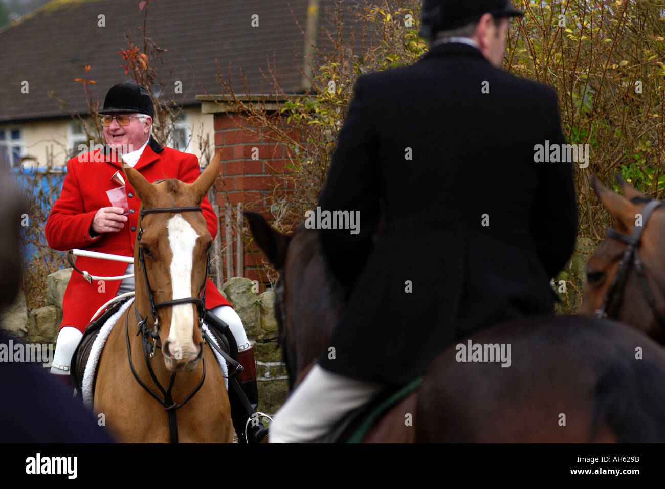 Huntsman in red coat on horseback with followers gather for fox hunt meeting in UK Stock Photo