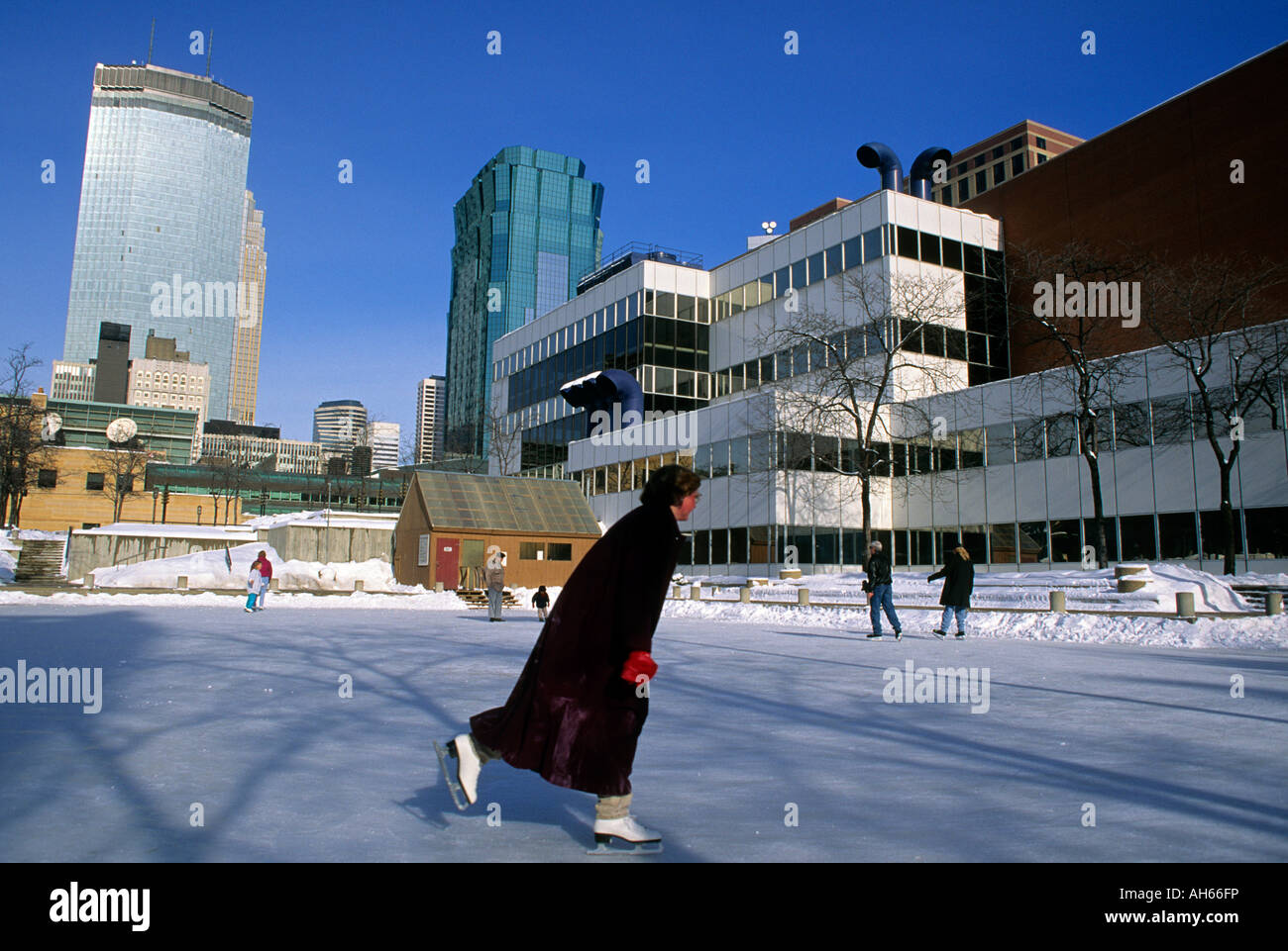 ICE SKATING ON THE PEAVEY PLAZA RINK IN DOWNTOWN MINNEAPOLIS, MINNESOTA.  ORCHESTRA HALL AND SKYLINE IN BACKGROUND.  FEBRUARY. Stock Photo