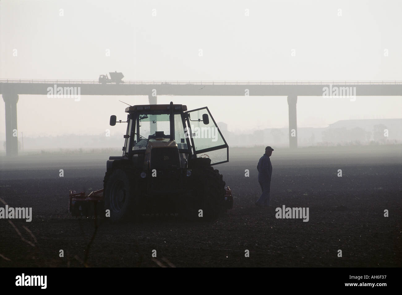 Misty day with farmer leaving tractor in field with lorry crossing road
