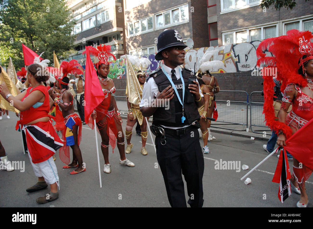 Young black police officer taking part in Notting Hill annual carnival as performers  dance and tease him. Stock Photo