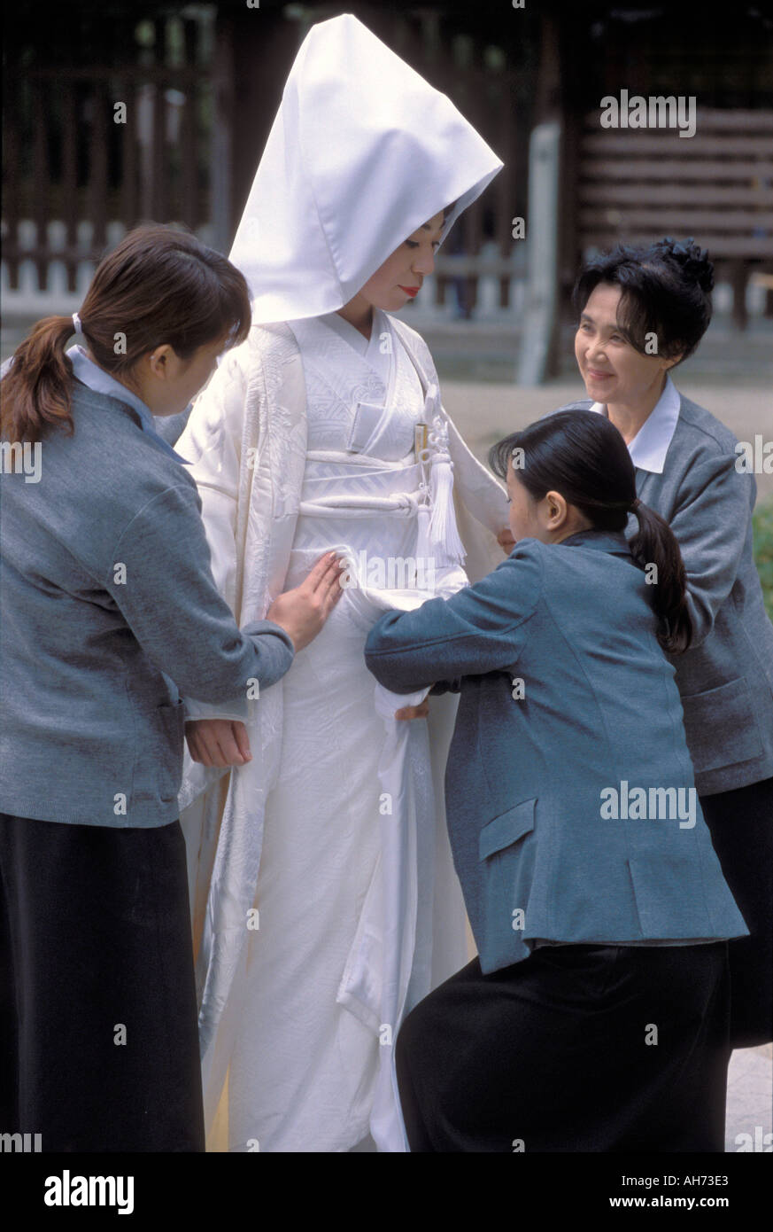 Three assistants fussing with the bride's white kimono worn during a traditional wedding ceremony Stock Photo