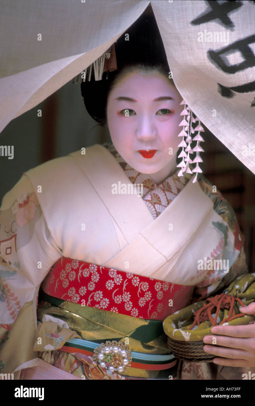 A tourist dressed as a maiko, or geisha in training, posing at a doorway curtain on her way outside Stock Photo