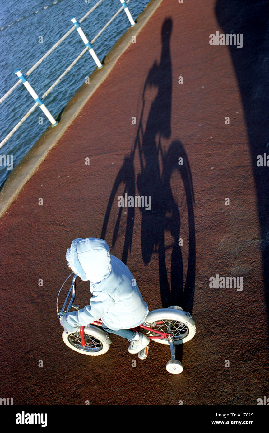 A child on a bicycle fitted with stabilisers casting a shadow Stock Photo