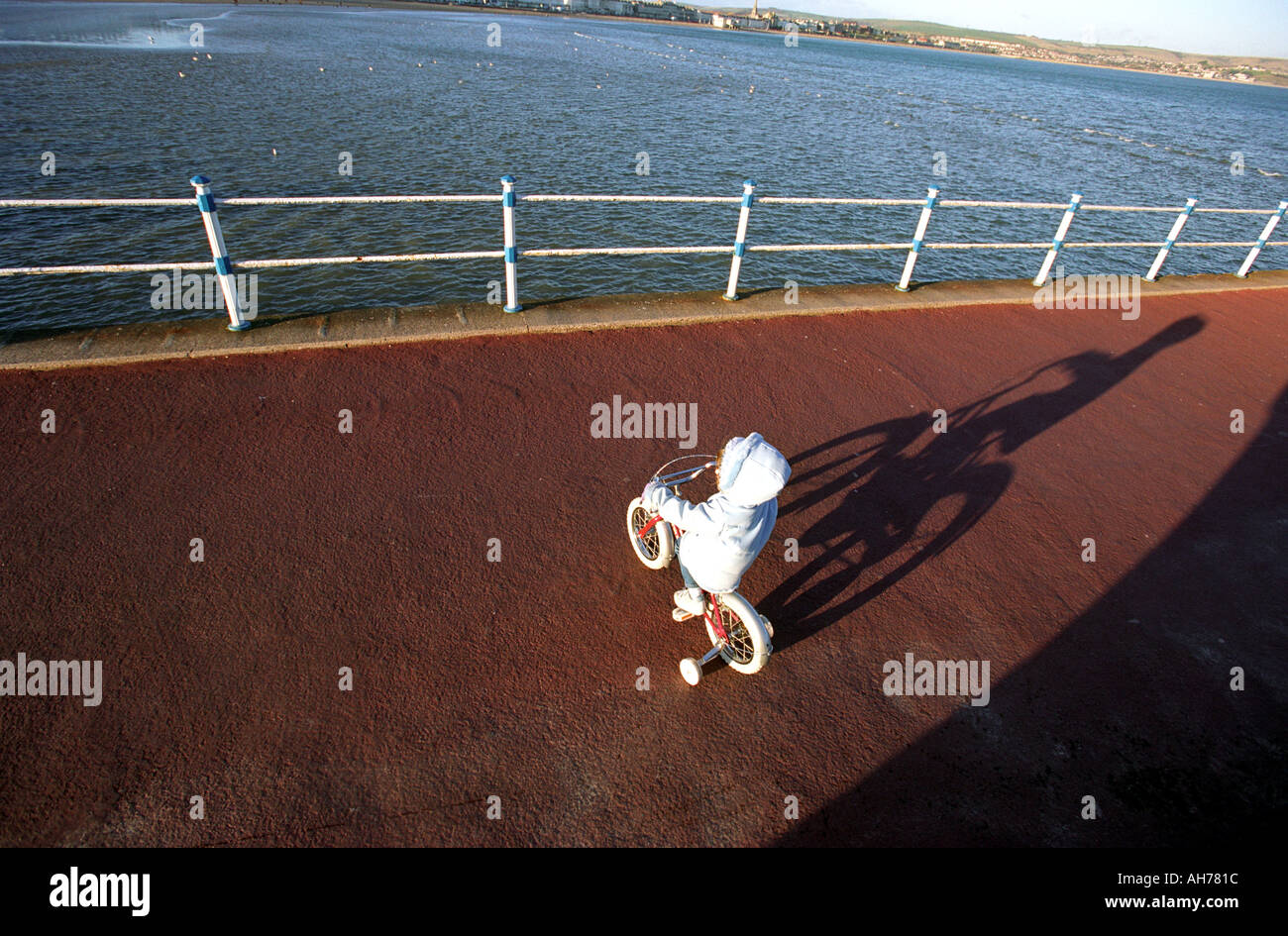A child on a bicycle fitted with stabilisers casting a shadow Stock Photo