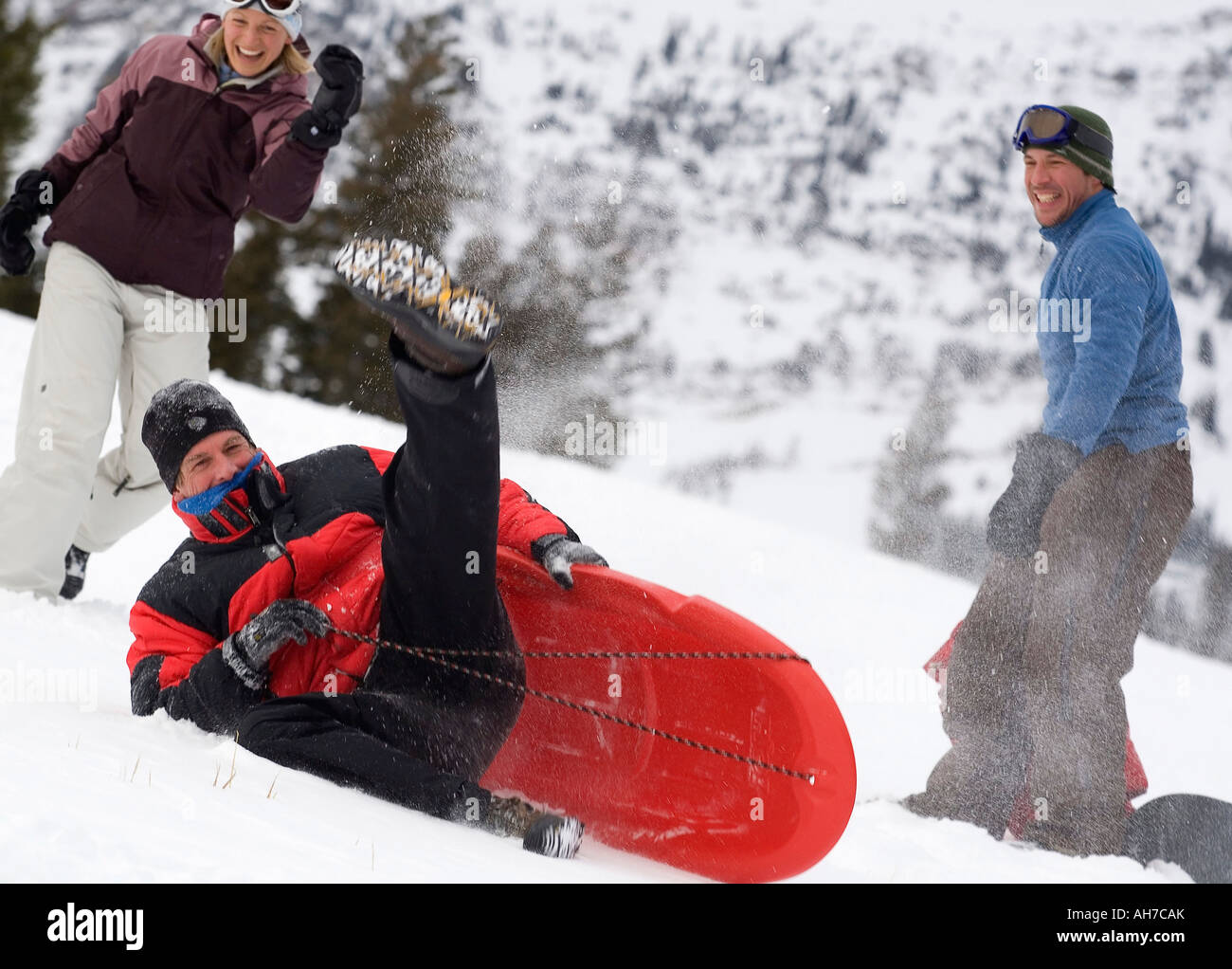 Mid adult man falling from a sled with a mid adult man and mid adult woman watching Stock Photo