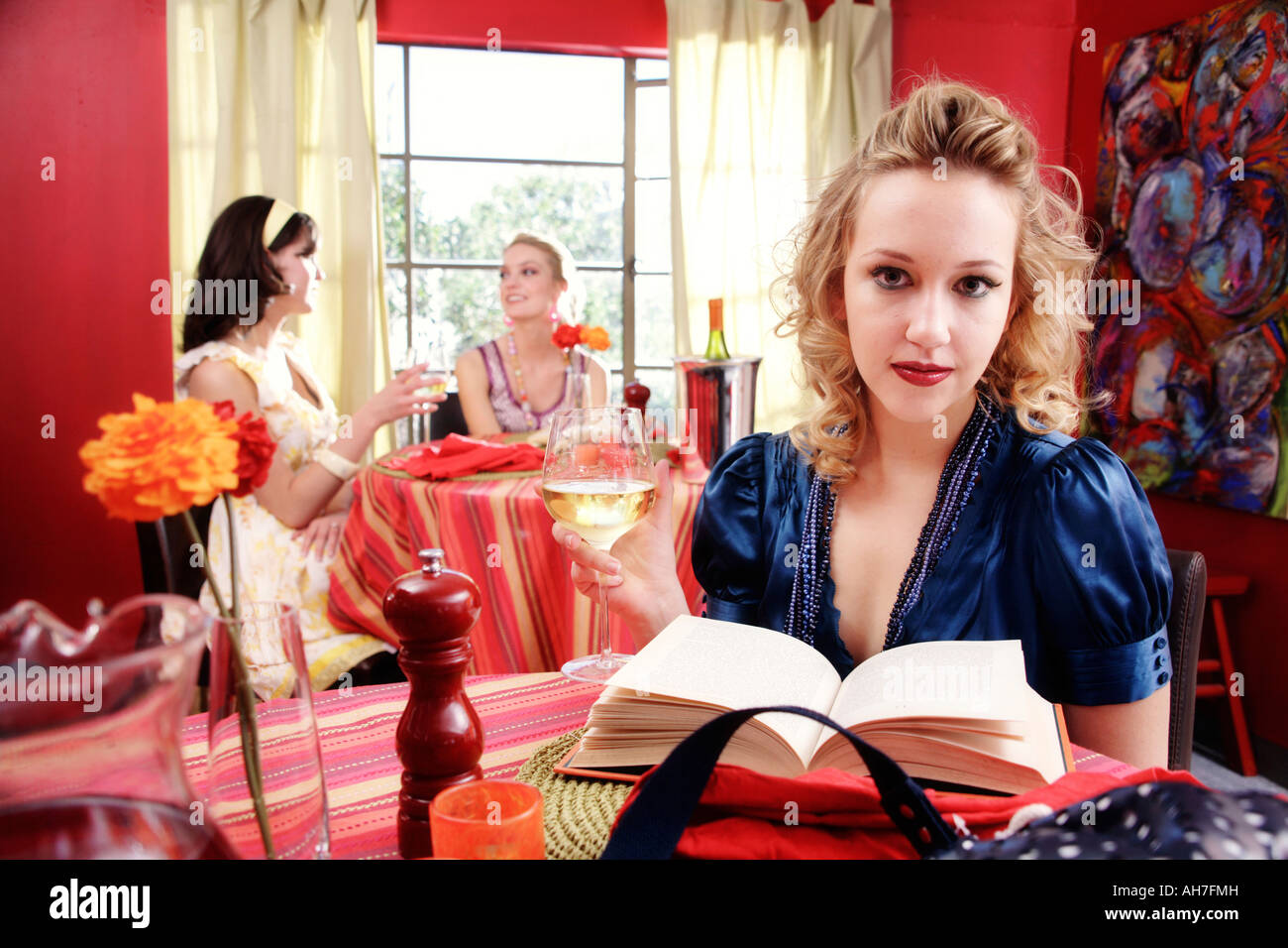 Young woman holding a wineglass with two young women dining in a restaurant behind her Stock Photo