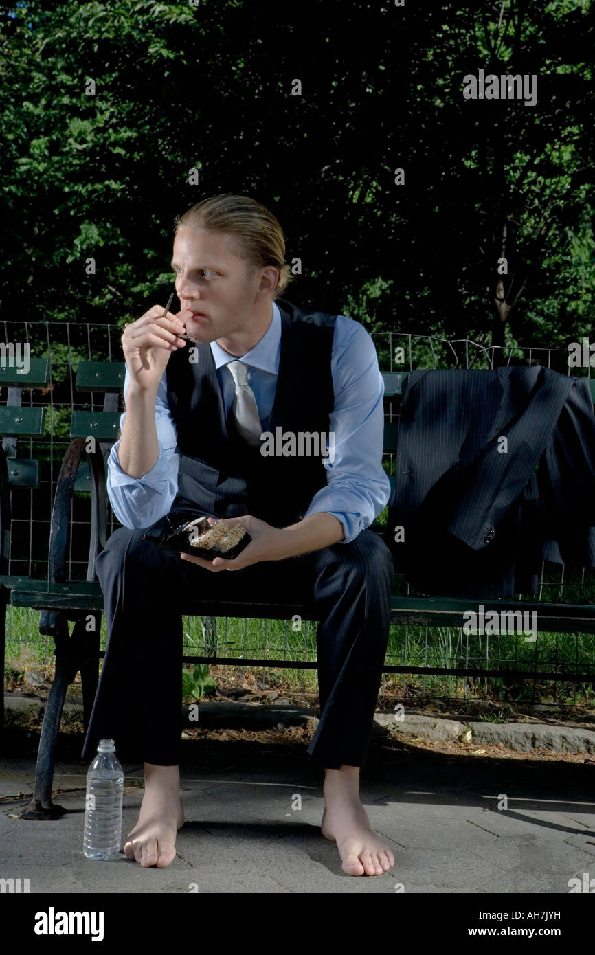 Businessman sitting on a park bench and eating food Stock Photo