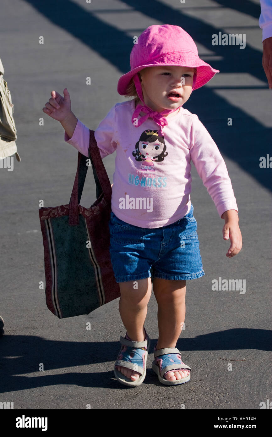 Toddler girl in a pink outfit walking while holding a bag that is too big for her, playing grownup in carrying her mother's bag Stock Photo