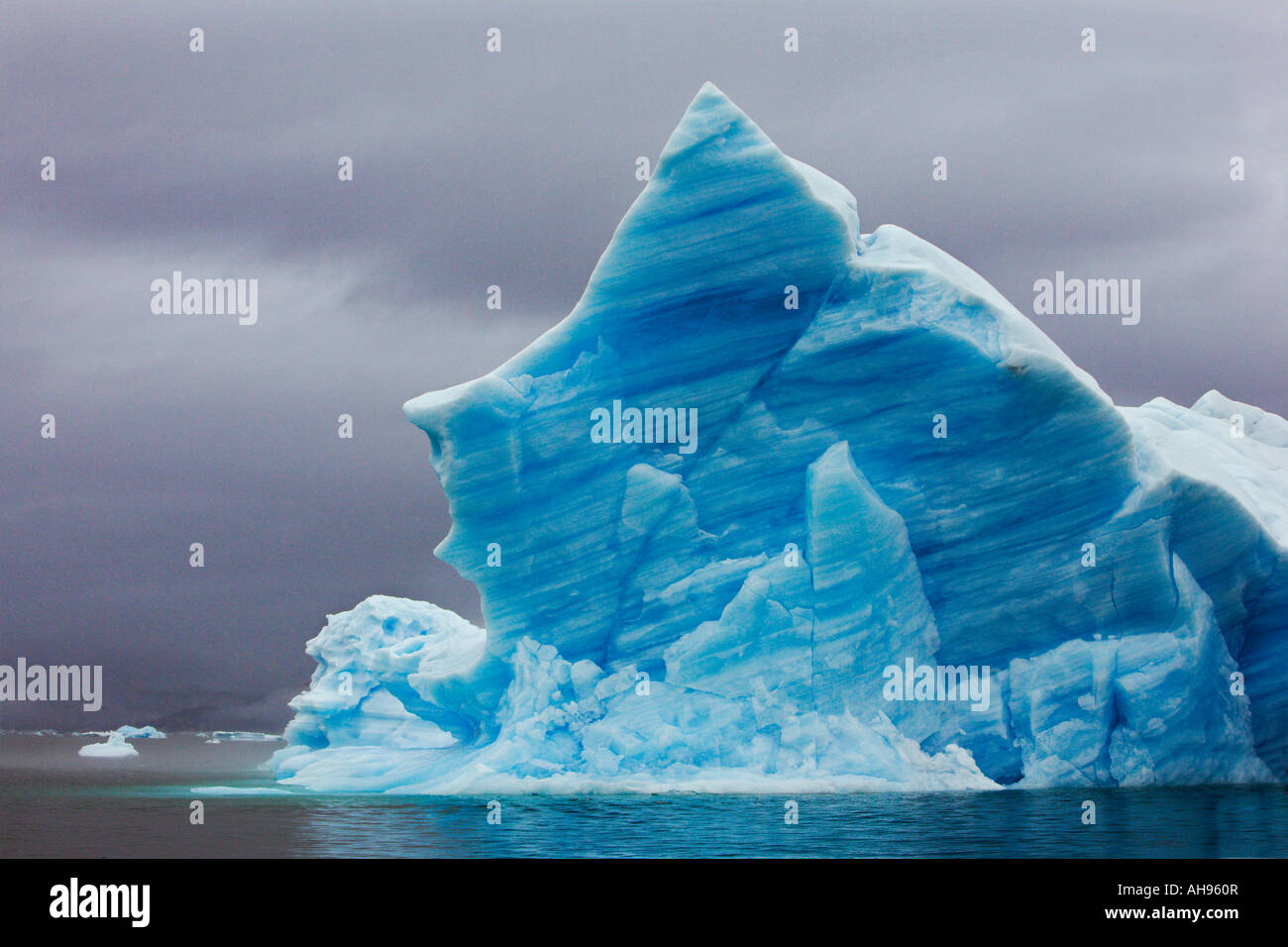 Huge beautiful classic blue pointed iceberg as typically found at Narsaq with rainy grey sky on the west coast of Greenland Stock Photo