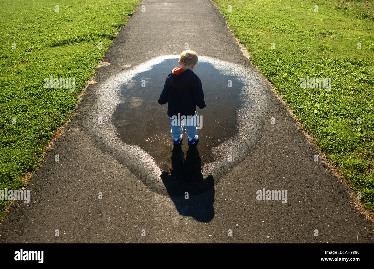 small boy looking down at puddle and shadow along a walkway Stock Photo