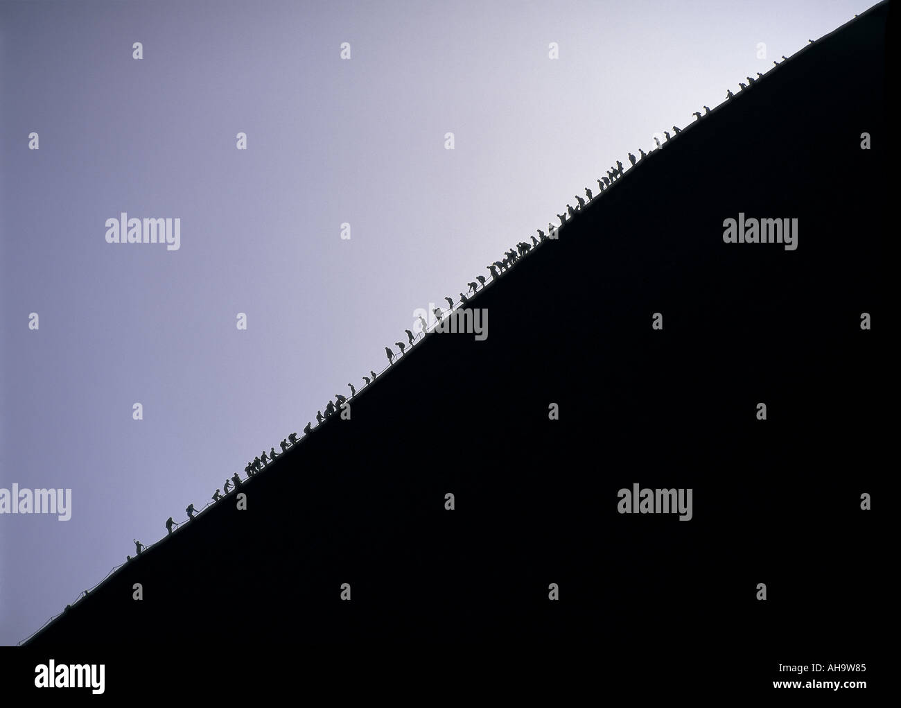 Tourists in silhouette climb Ayers Rock at dawn, Australia Stock Photo