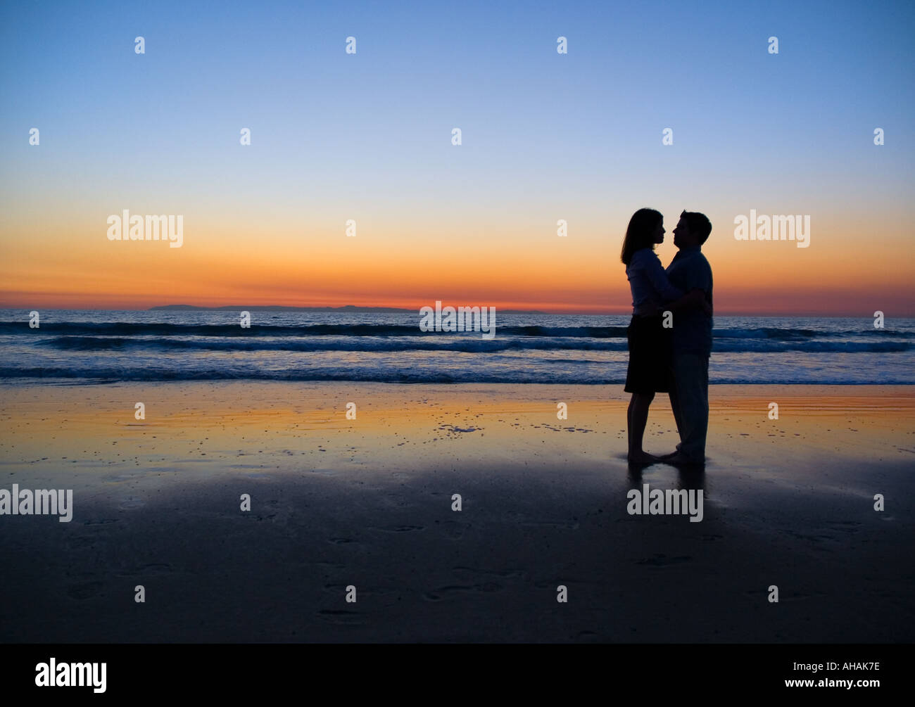 A romantic couple silhouetted by a glowing sunset on a beach Stock Photo