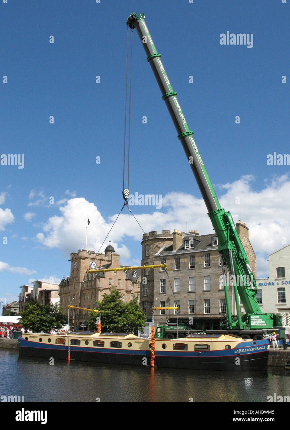Heavy crane lifting a narrow boat into the water on the Shore at Stock