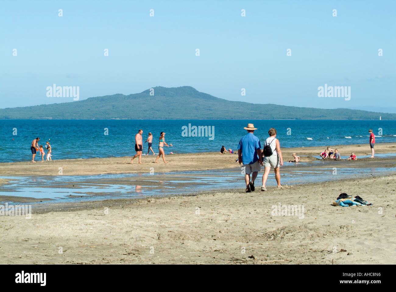 A couple walk along the beach at Mairangi Bay with Rangitoto Island a