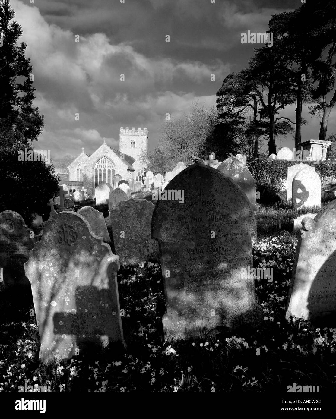 Very atmospheric high contrast mono image of churchyard with early morning sunlight illuiminating the church as if glowing Stock Photo