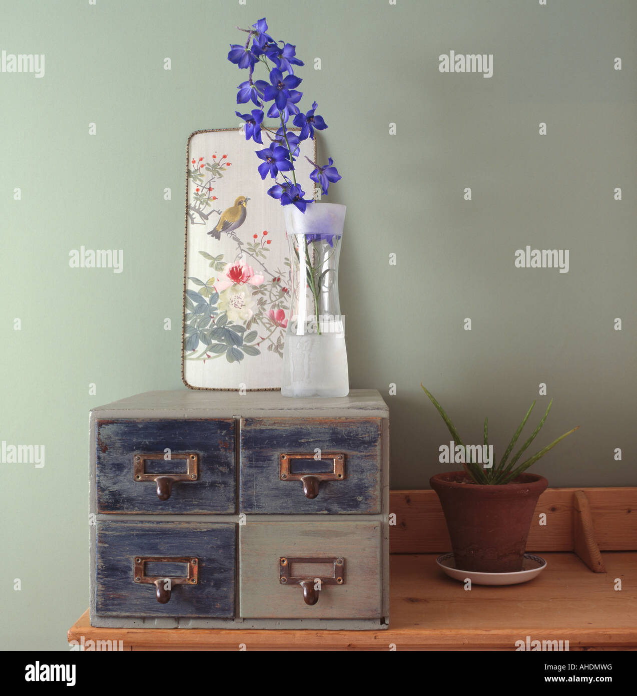 Close up of small Chinese picture and single blue delphinium flower in glass vase on set of small filing drawers Stock Photo