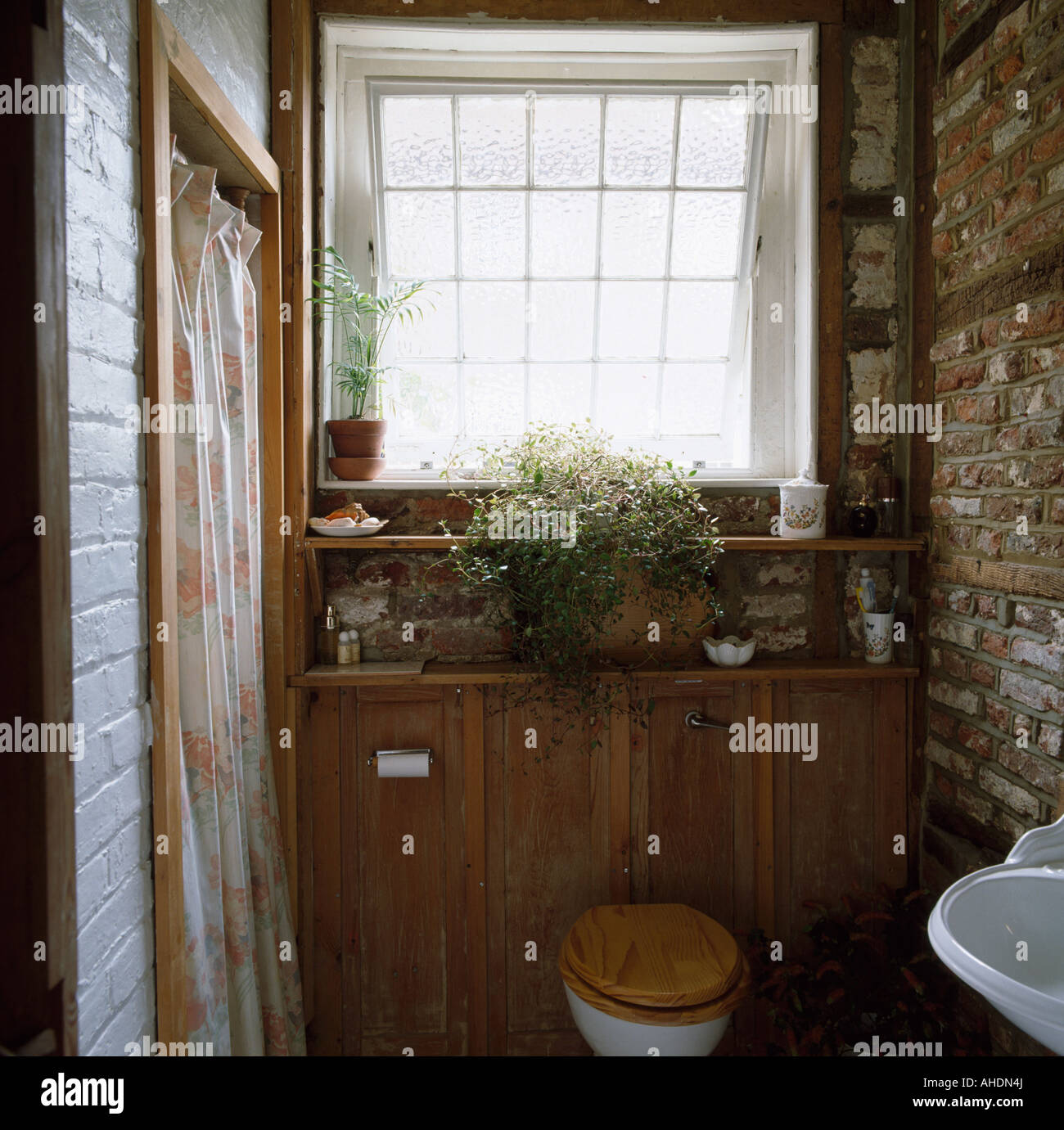 Toilet with wooden seat in small cloakroom with exposed brick wall