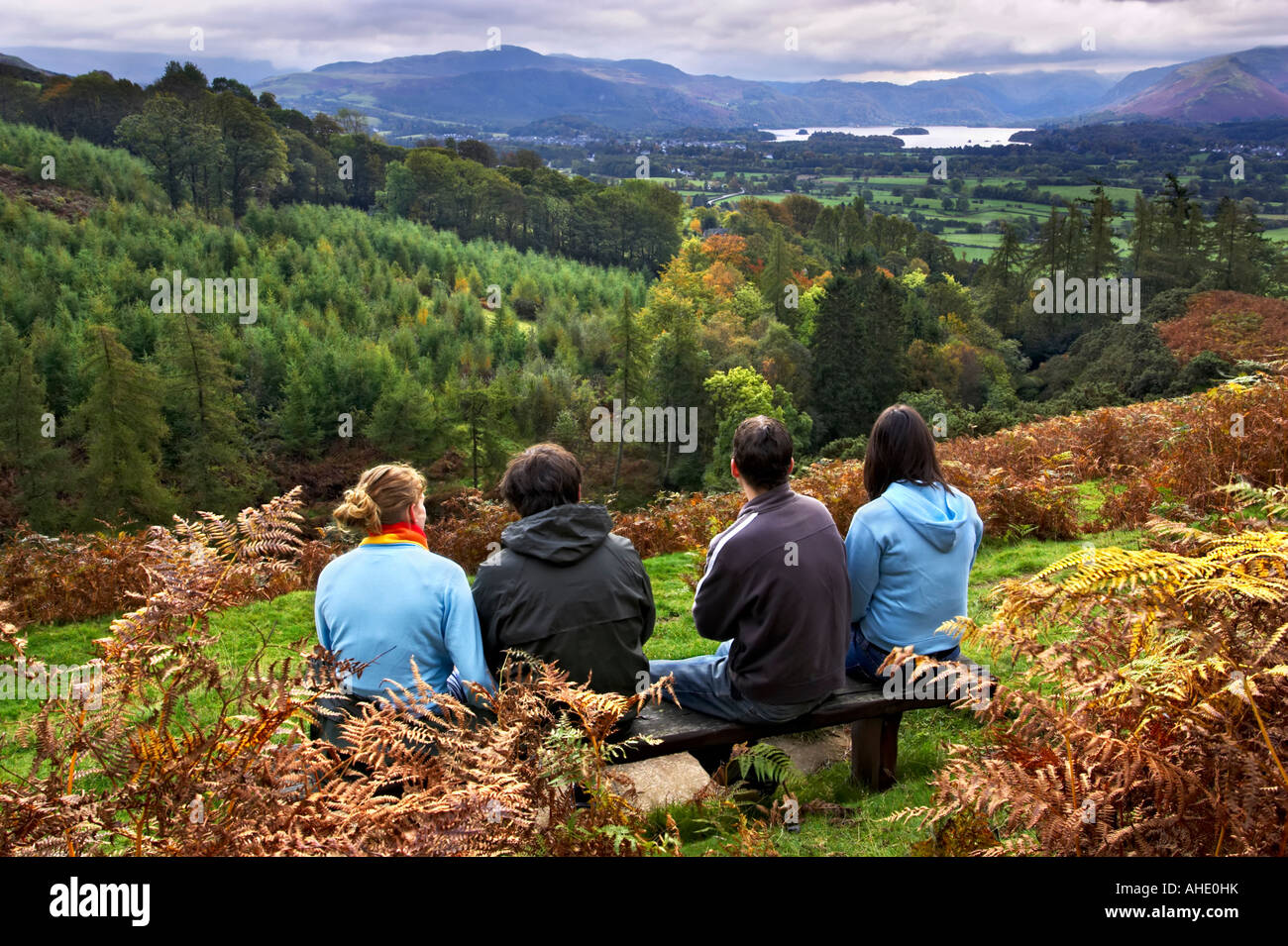 Four mid 20s hikers on a bench on the lower slopes of Skiddaw admiring the view of Derwent Water, Keswick & Borrowdale. Stock Photo