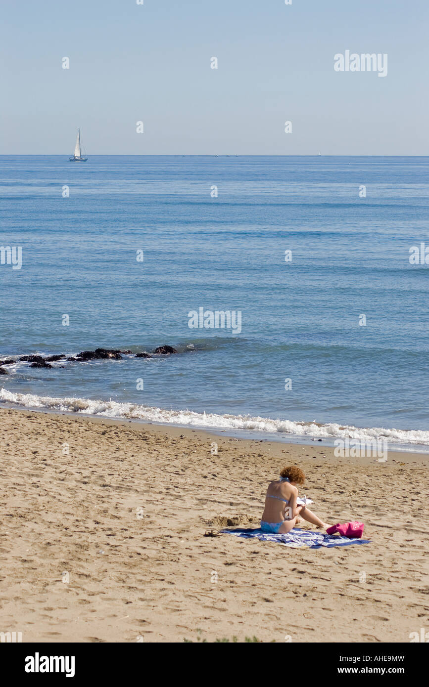Bikini clad woman reading a book on a sandy Spanish beach in the early