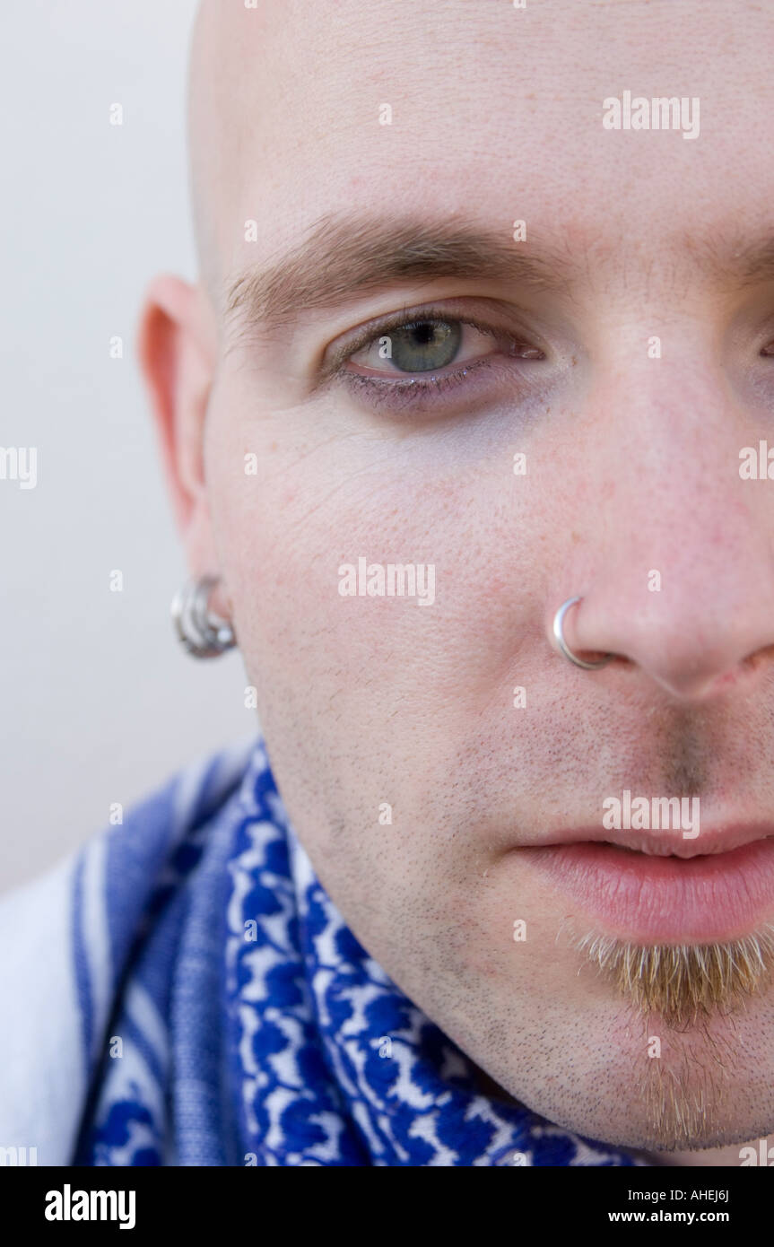close up of the right side of the face of a man with shaved head and pierced nose and ears and small goatee beard Stock Photo