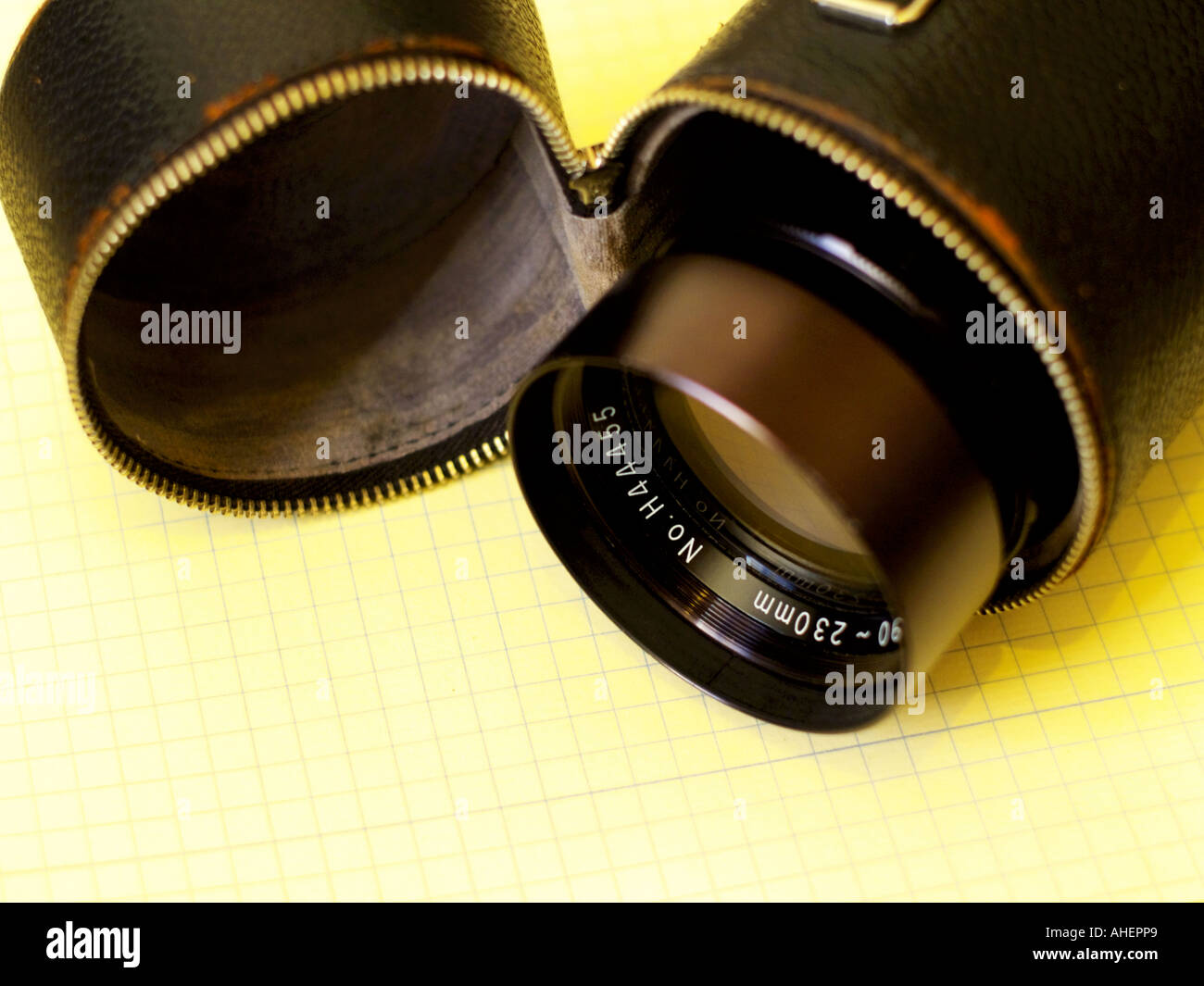 Vintage telephoto lens and case atop faint yellow grid with cross